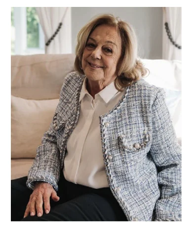 Fausta Fontana, seated on a sofa in a pale tweed jacket, smiling